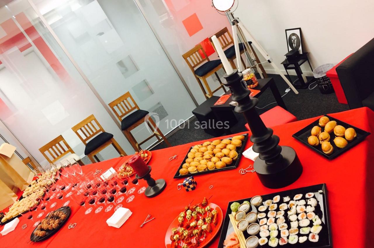 Buffet varié avec sushis, amuse-bouches et desserts, disposé sur une table rouge dans une salle moderne.