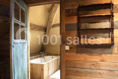 Salle de bain avec lavabo moderne, douche vitrée et miroir, dans une pièce aux poutres apparentes en bois.