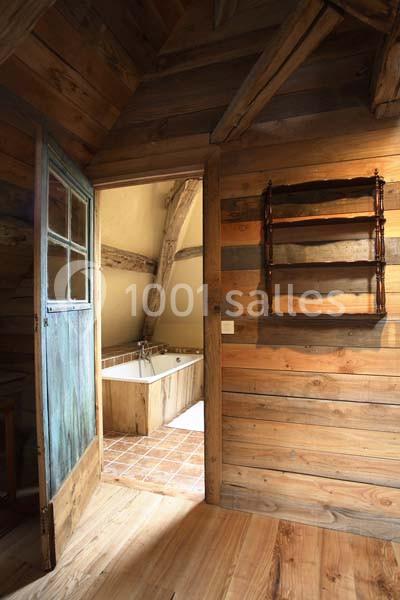 Vue d'une salle de bain rustique avec baignoire en bois, murs en bois et étagères murales dans une pièce chaleureuse.