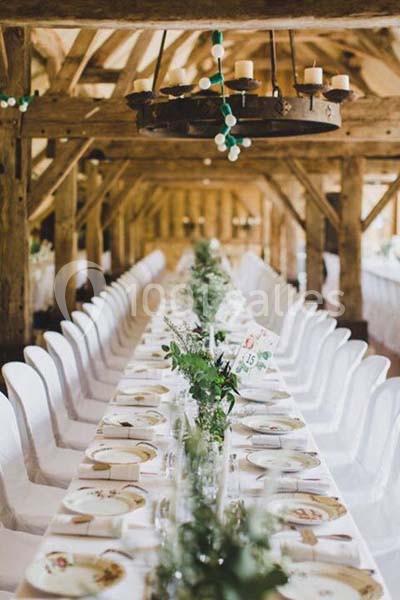 Grande table de banquet décorée de verdure et de vaisselle, installée dans une salle en bois avec poutres apparentes.
