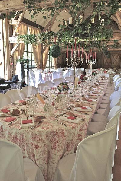 Table de banquet élégamment dressée dans une salle rustique avec poutres apparentes et décoration florale suspendue.