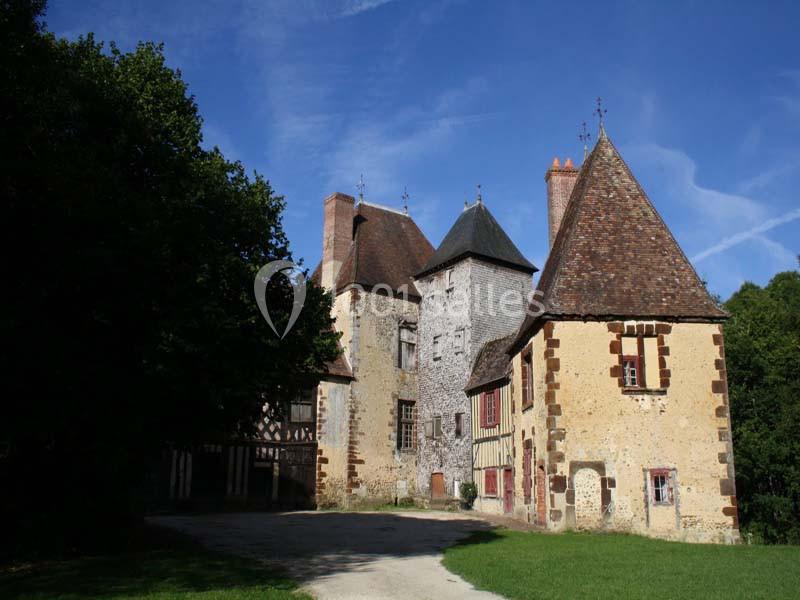 Bâtiment ancien en pierre et à colombages, entouré d'arbres, sous un ciel bleu dégagé.