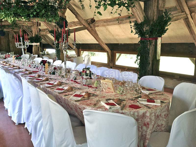 Grande table de banquet décorée avec nappes fleuries, chandeliers, vaisselle élégante et chaises blanches dans une salle…
