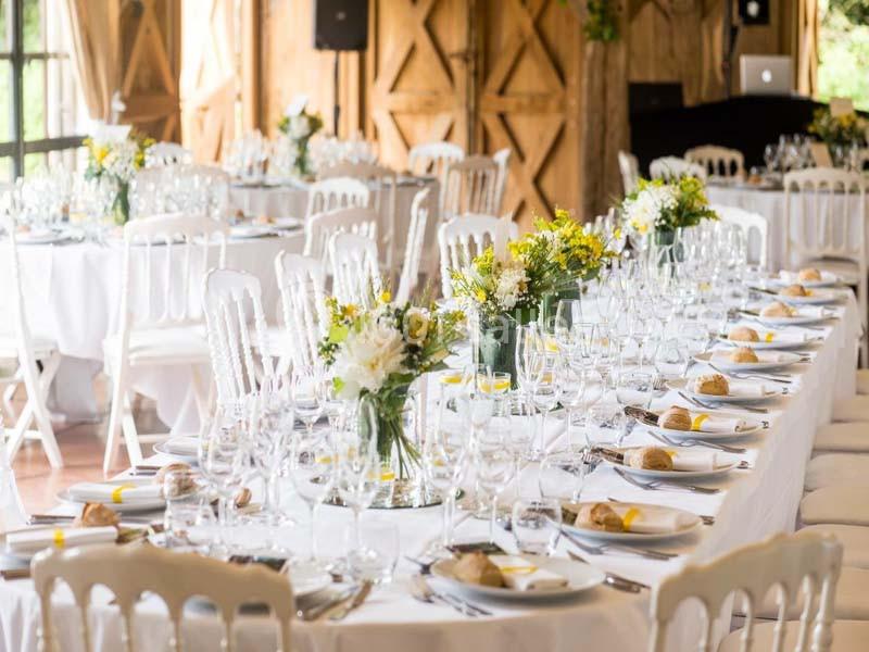 Tables de réception élégamment dressées avec nappes blanches, vaisselle, verres et arrangements floraux.