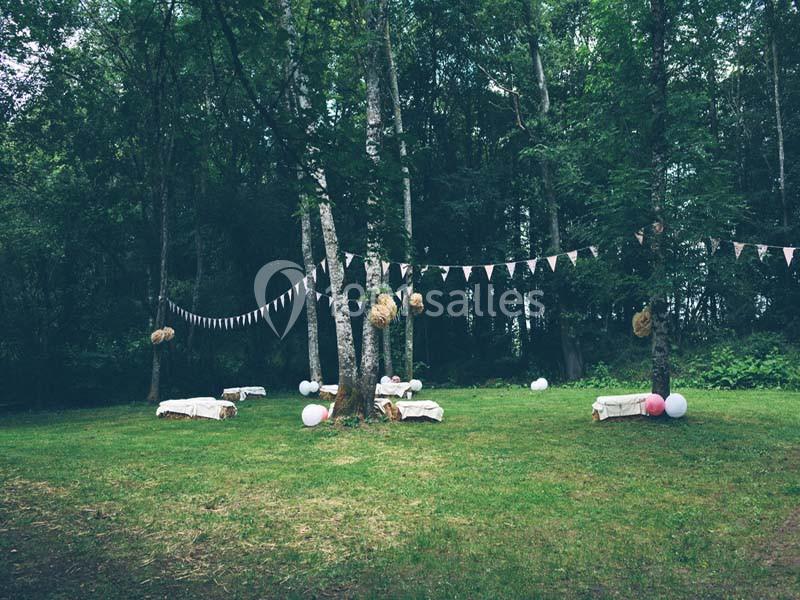 Un espace extérieur boisé décoré de guirlandes, ballons et bancs recouverts de tissu, idéal pour un événement.