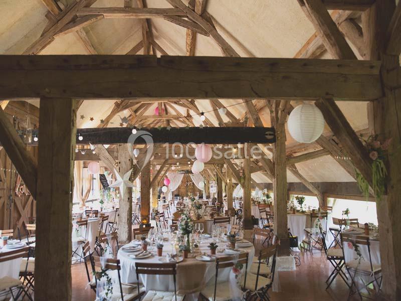 Salle de réception rustique avec poutres apparentes, tables décorées et lanternes suspendues.