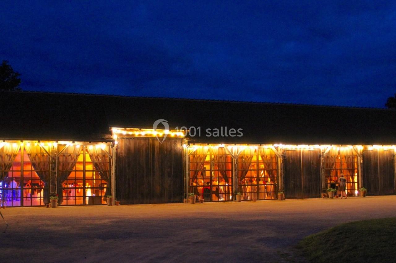 Grange en bois éclairée par des guirlandes lumineuses, avec des fenêtres laissant entrevoir une ambiance festive à l…