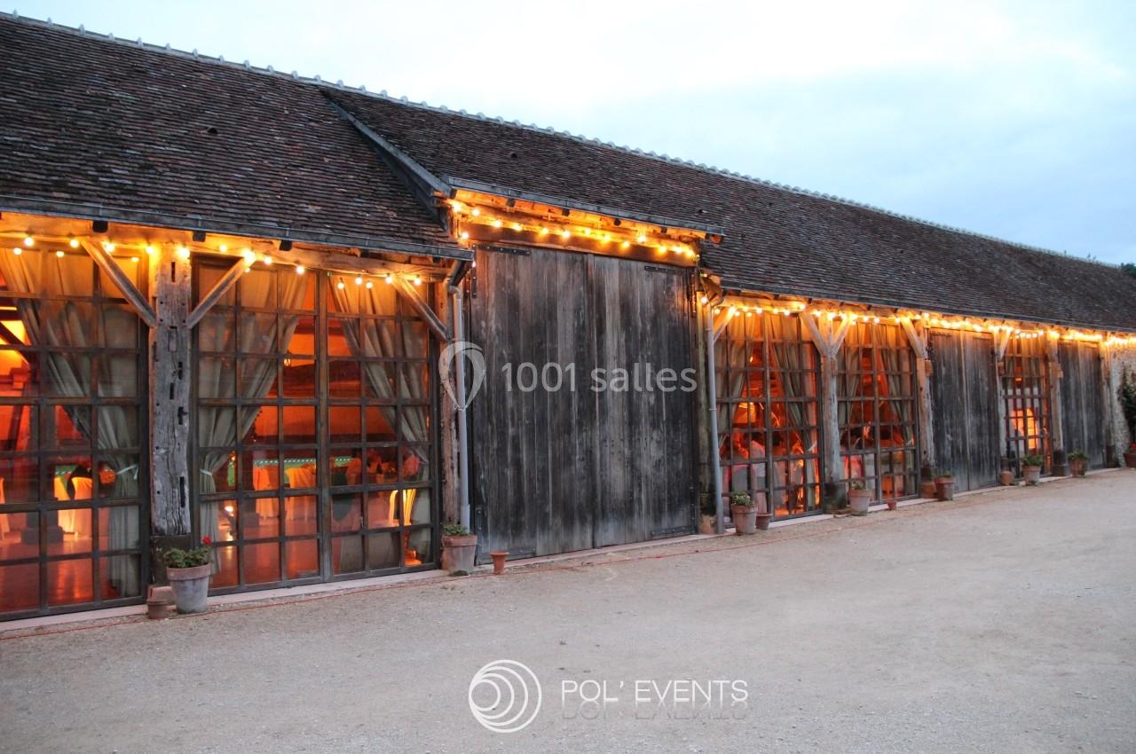 Grange en bois avec grandes baies vitrées éclairées par des guirlandes lumineuses, en soirée.
