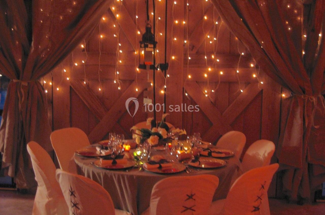 Table ronde décorée pour un dîner, entourée de chaises blanches, devant un rideau illuminé de guirlandes lumineuses.