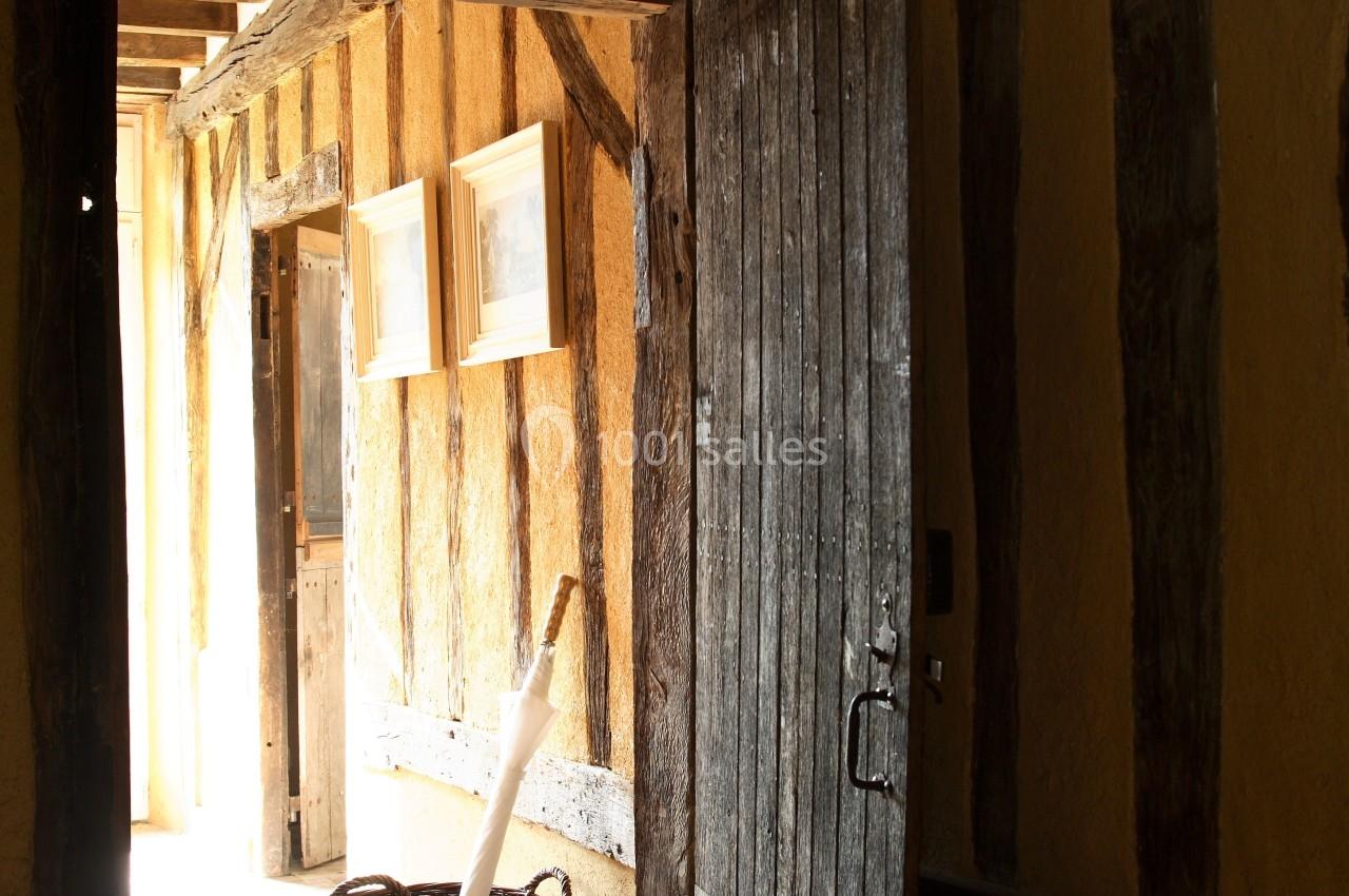 Porte en bois ouverte sur un couloir lumineux avec murs en colombages, panier en osier posé au sol.