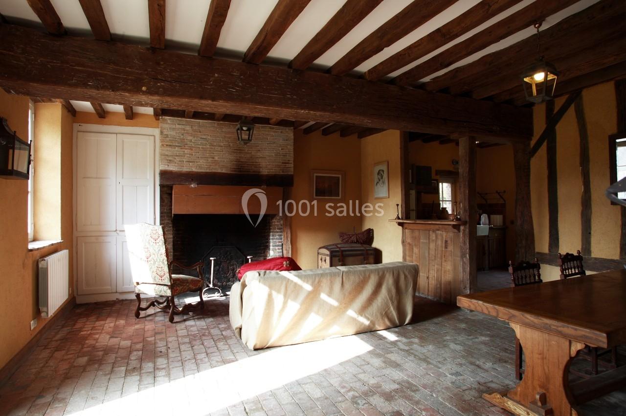 Salon rustique avec poutres apparentes, cheminée en briques, mobilier ancien et sol en carreaux de terre cuite.