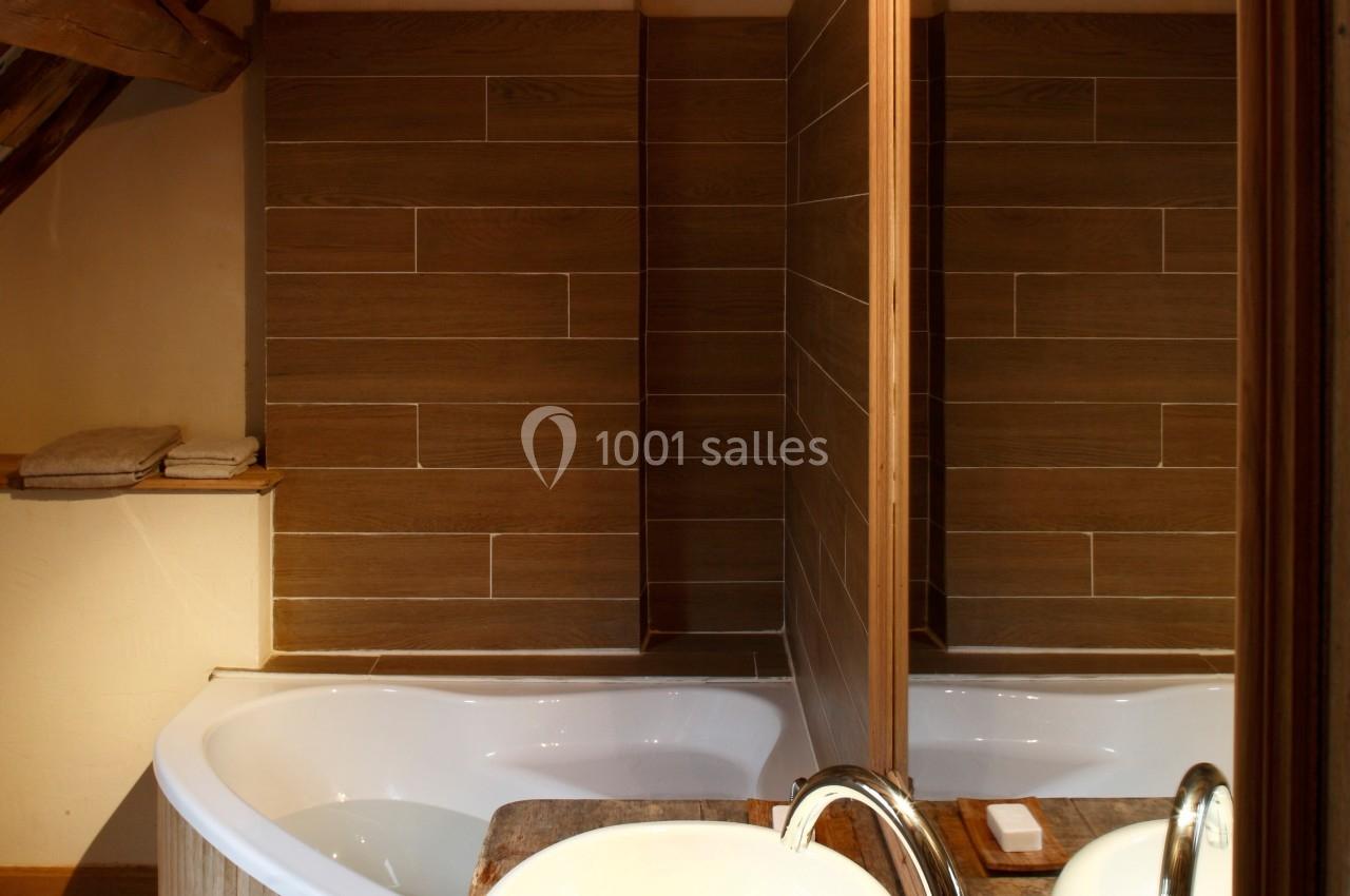 Salle de bain avec baignoire d'angle, vasque ronde sur plan en bois, miroir et murs en carrelage effet bois.