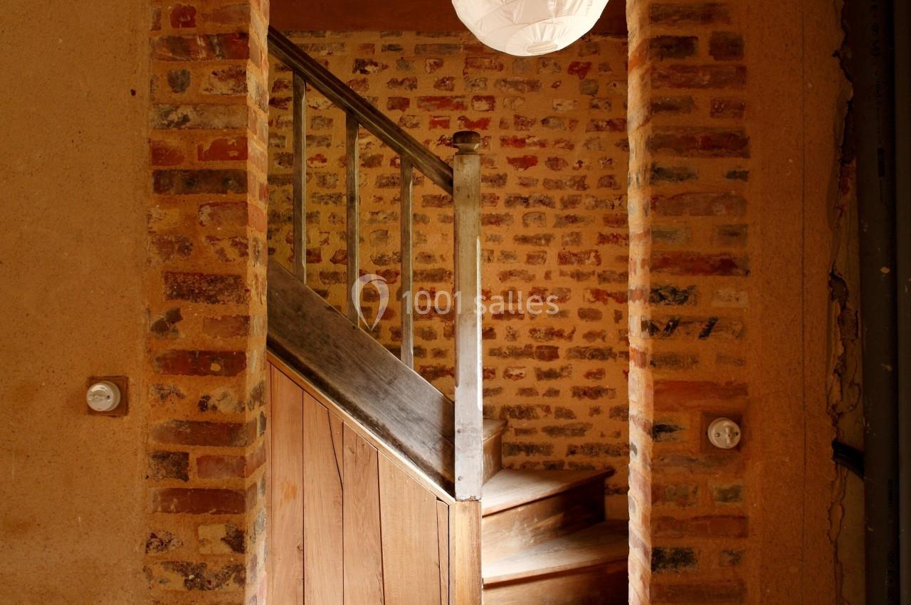 Vue d'un escalier en bois entouré de murs en briques dans une maison au style rustique.