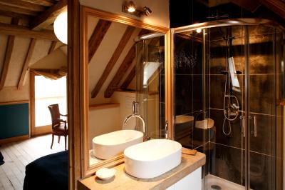 Salle de bain avec lavabo moderne, douche vitrée et miroir, dans une pièce aux poutres apparentes en bois.