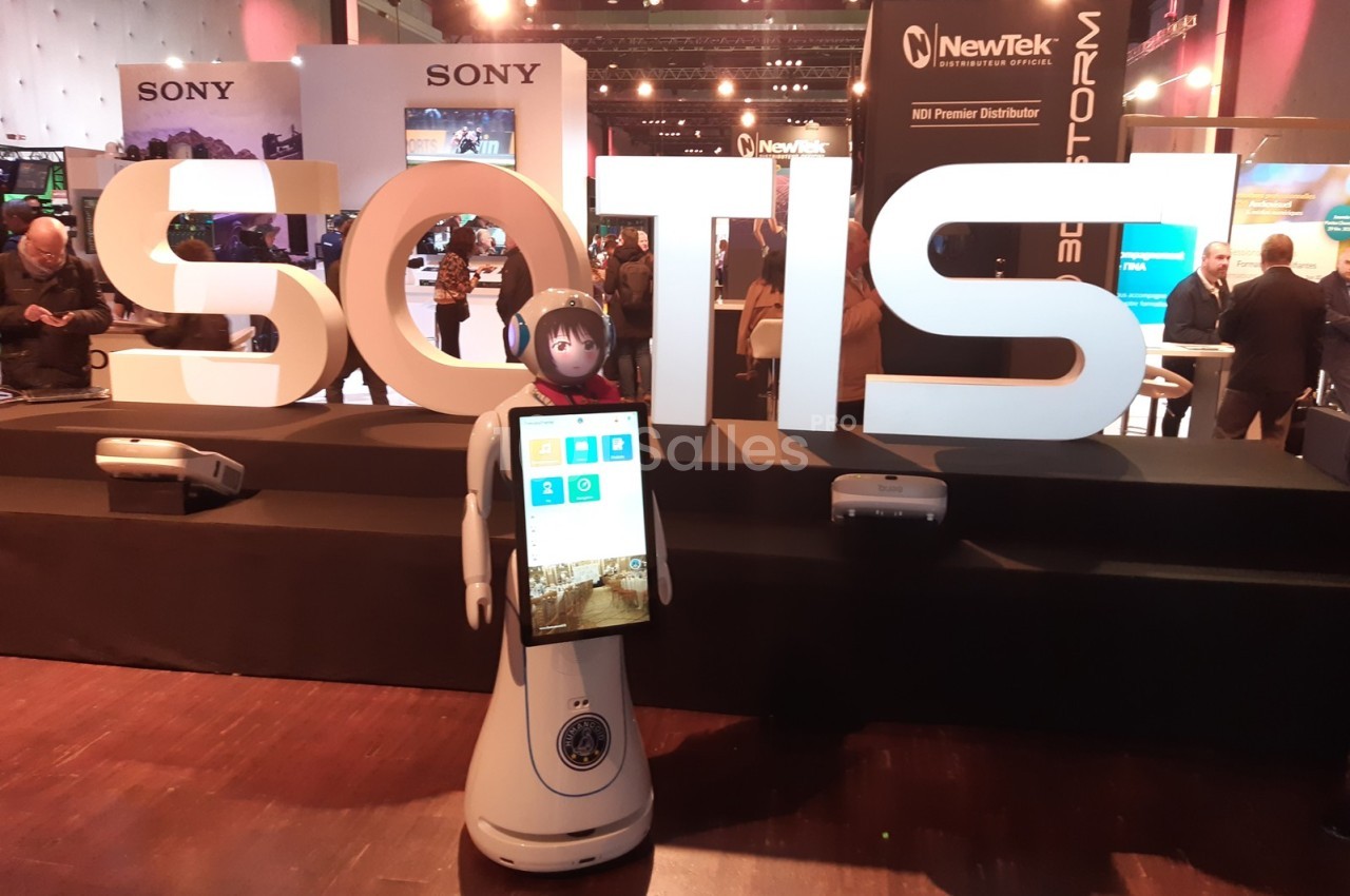 Un robot humanoïde avec écran tactile devant un stand marqué ’SOTIS’ dans un salon technologique.