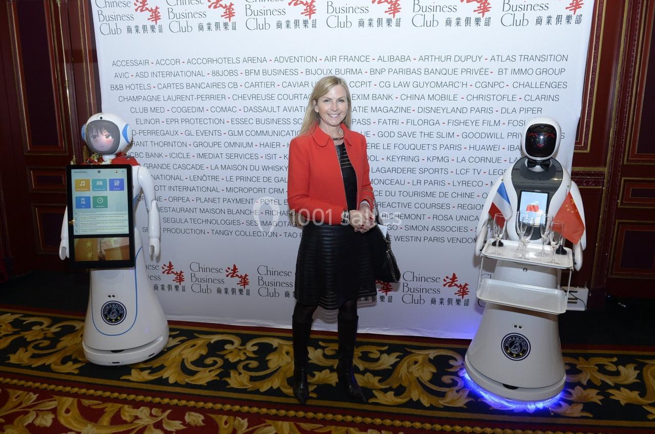 Une femme pose entre deux robots humanoïdes dans un cadre formel avec une bannière d'événement en arrière-plan.