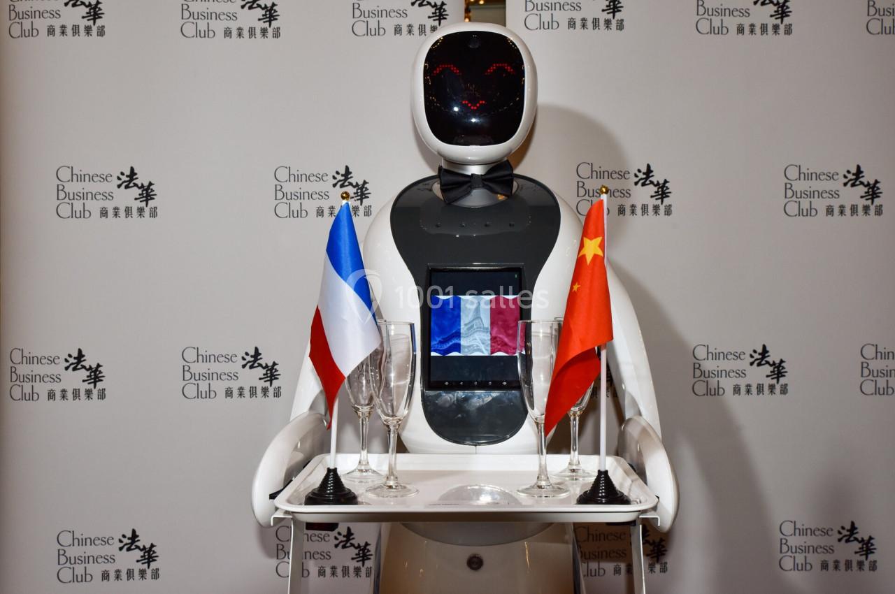 Un robot humanoïde portant un plateau avec des drapeaux français et chinois, devant un fond marqué ’Chinese Business Club’.