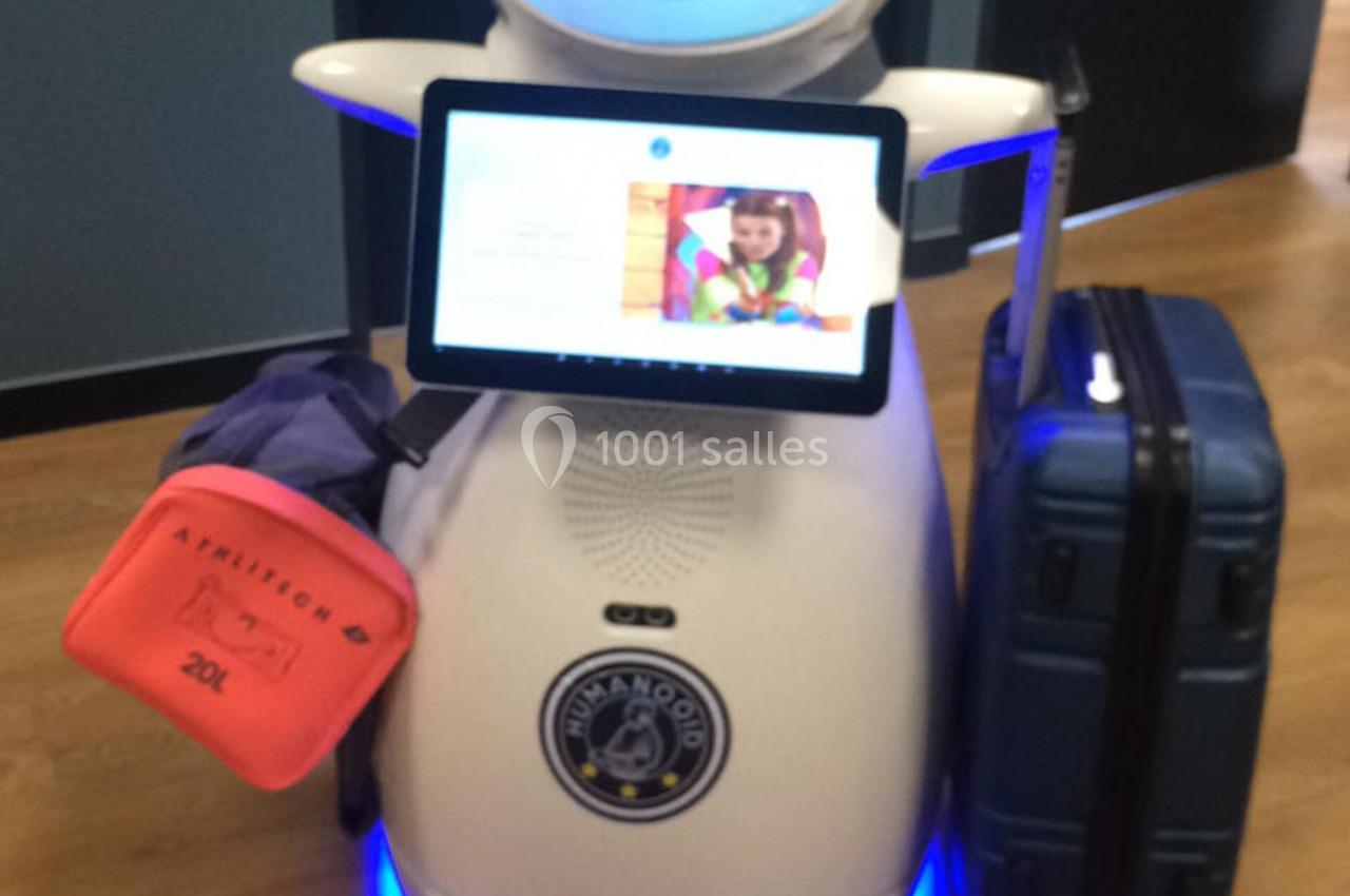 Robot blanc avec un écran affichant une interface, transportant des bagages sur un sol en bois.