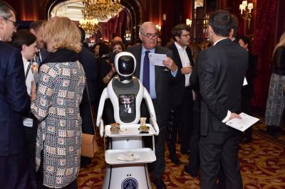 Robot humanoïde blanc équipé d'un écran et d'un plateau, présenté dans un environnement intérieur avec plantes et…