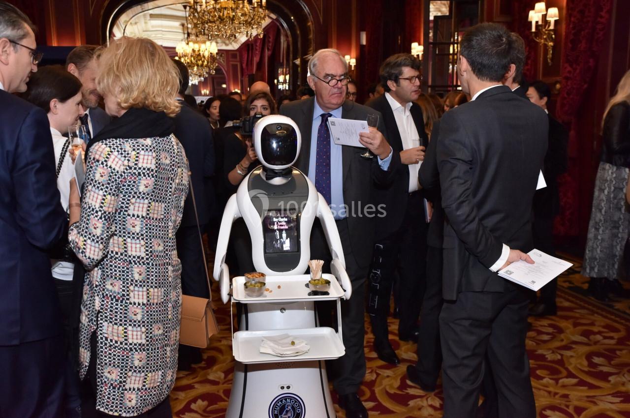 Un robot équipé d'un plateau sert des boissons et des amuse-bouches lors d'un événement dans un cadre élégant.