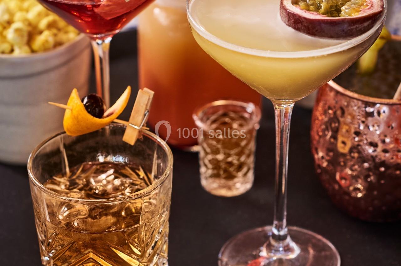 Plateau de cocktails variés avec garnitures, accompagné de popcorn et d'un verre en cuivre sur une table en mosaïque.