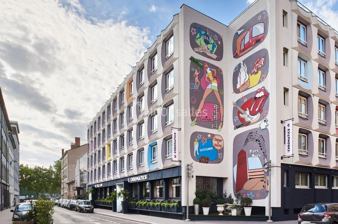 Façade d'un immeuble urbain décorée de fresques colorées, avec une rue bordée de voitures et de végétation.