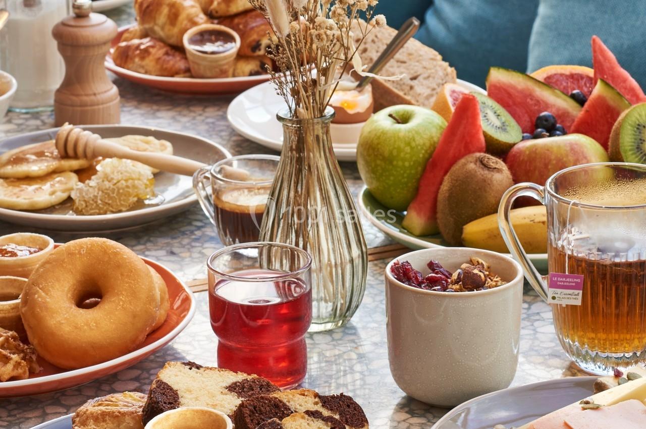 Petit-déjeuner varié avec viennoiseries, fruits frais, boissons et pain sur une table lumineuse et conviviale.