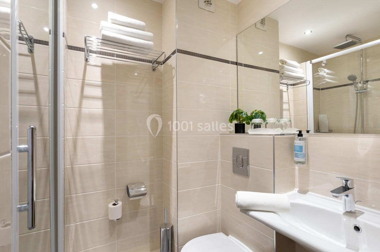 Salle de bain moderne avec douche, lavabo, miroir, toilettes et étagère murale garnie de serviettes pliées.