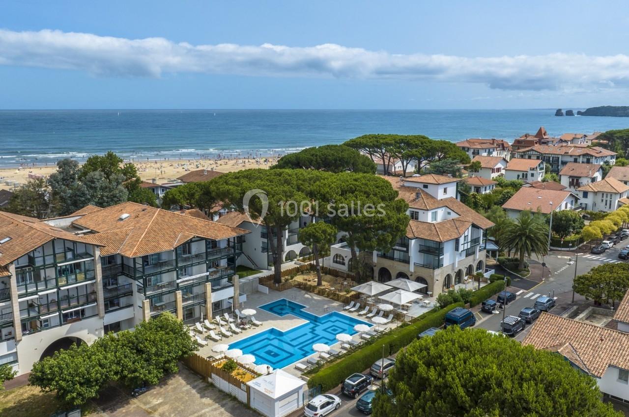 Vue aérienne d'un complexe résidentiel avec piscine, entouré de maisons et donnant sur une plage et l'océan.