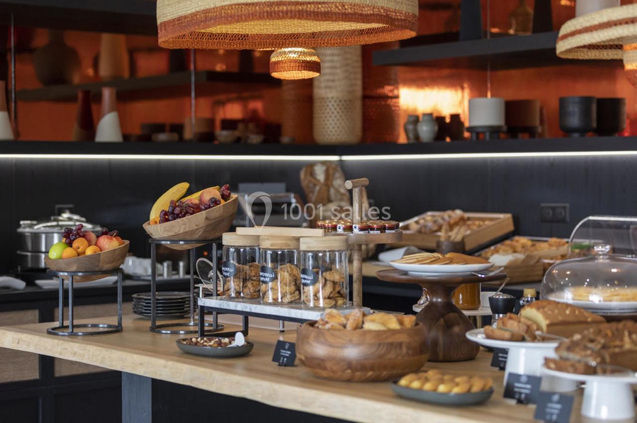 Buffet varié avec fruits, viennoiseries, biscuits et pains disposés sur une table en bois dans un cadre chaleureux.