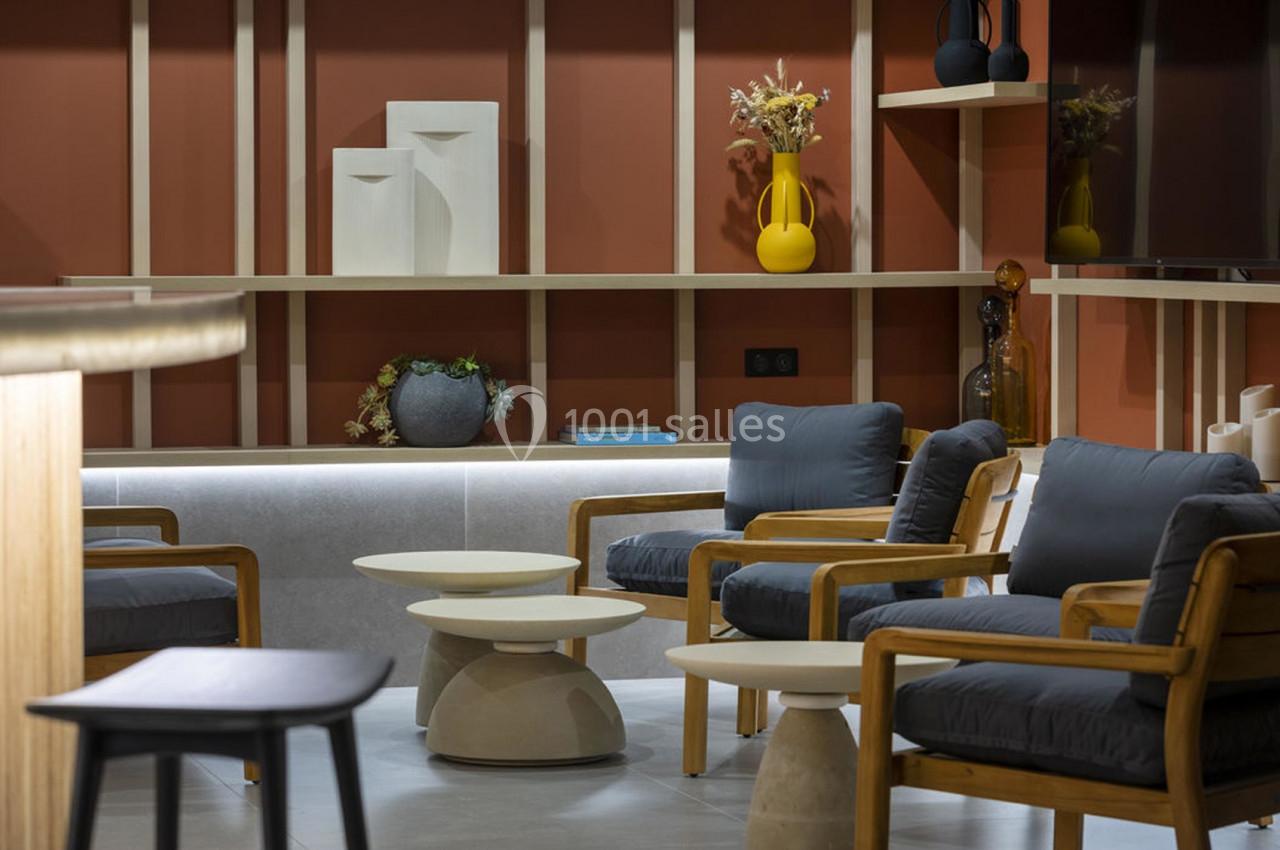 Espace salon moderne avec fauteuils en bois, tables basses design et étagères décorées d'objets et de vases colorés.