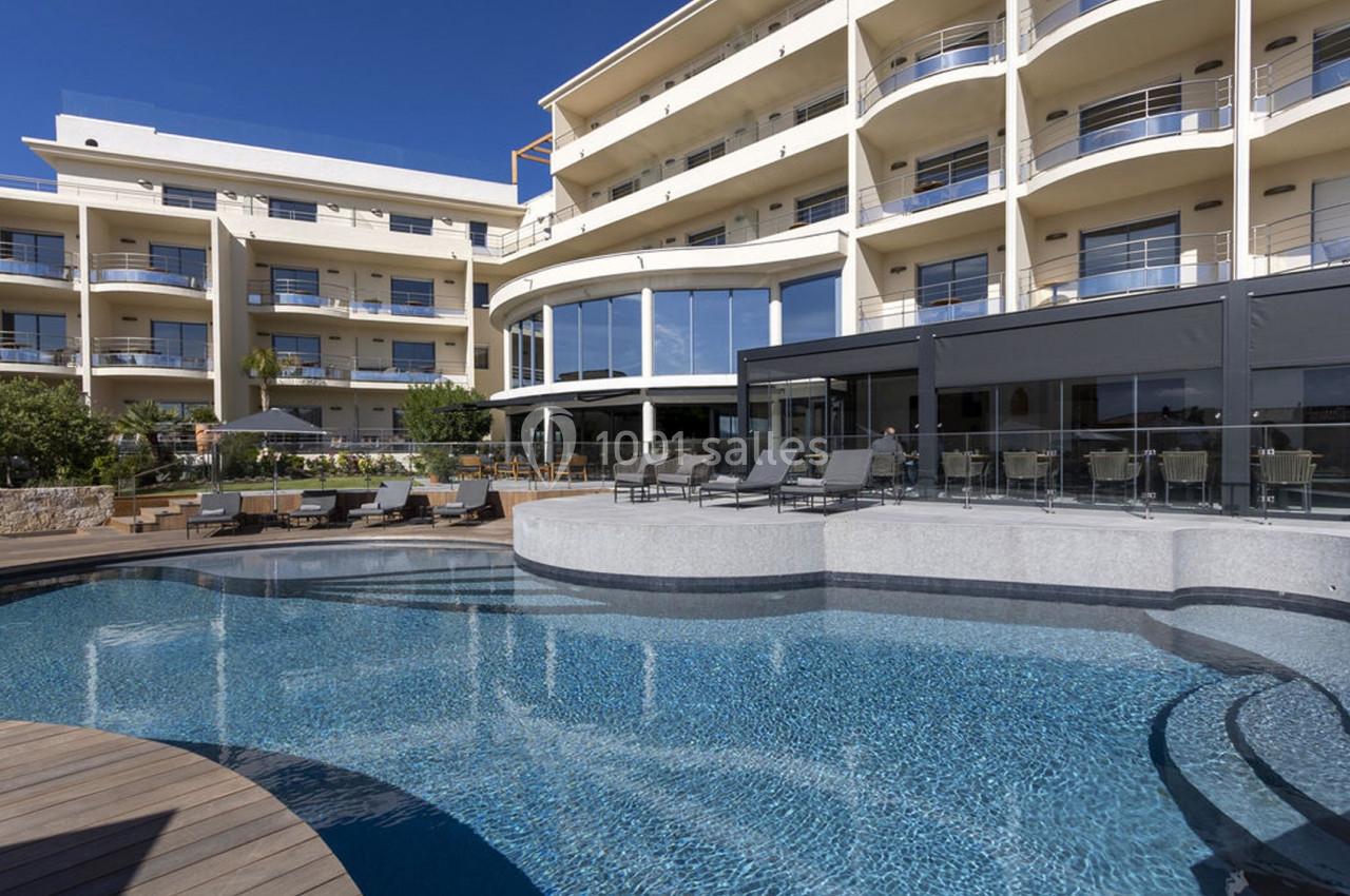 Vue d'une piscine extérieure entourée de chaises longues, devant un bâtiment moderne à plusieurs étages.