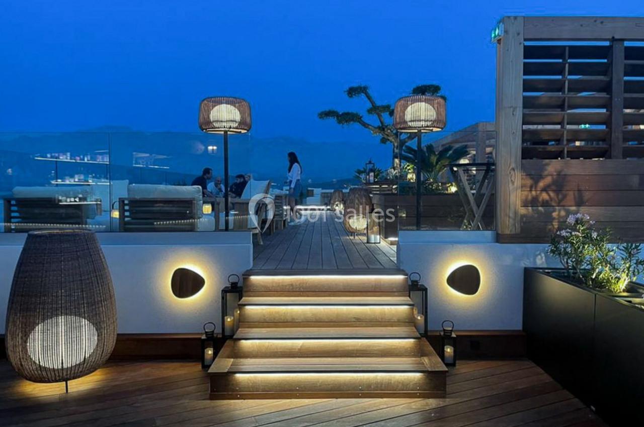 Terrasse en bois éclairée avec des lampes modernes, offrant une vue nocturne sur des montagnes et un ciel bleu profond.
