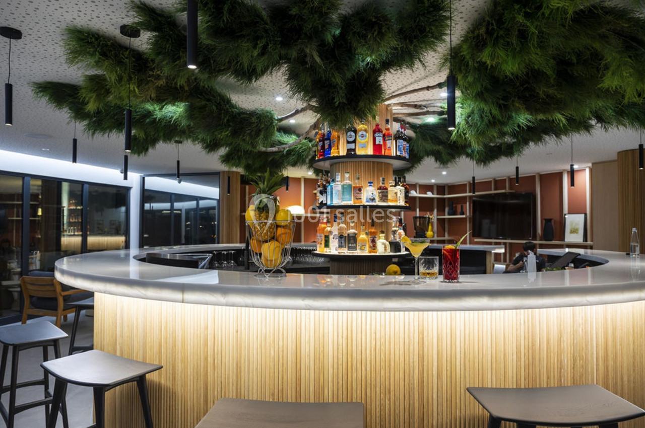 Bar circulaire moderne avec étagères de bouteilles, décoré de plantes suspendues et éclairage tamisé.