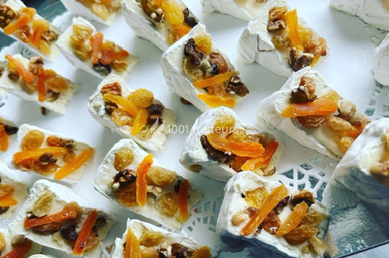 Morceaux de fromage garnis de fruits secs et d'abricots, disposés sur un plateau blanc.