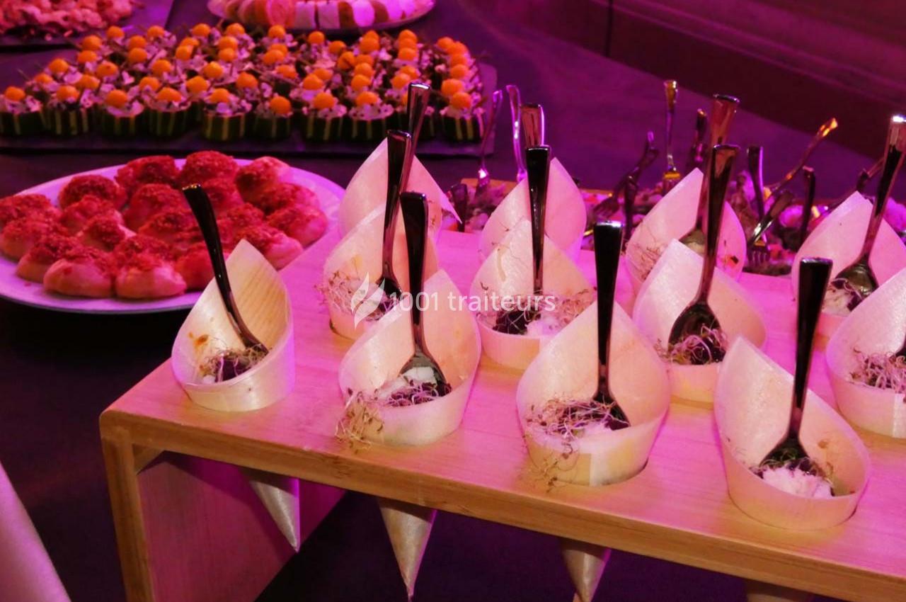 Présentoir de bouchées apéritives élégantes avec cuillères, entouré de plateaux de petits fours variés.