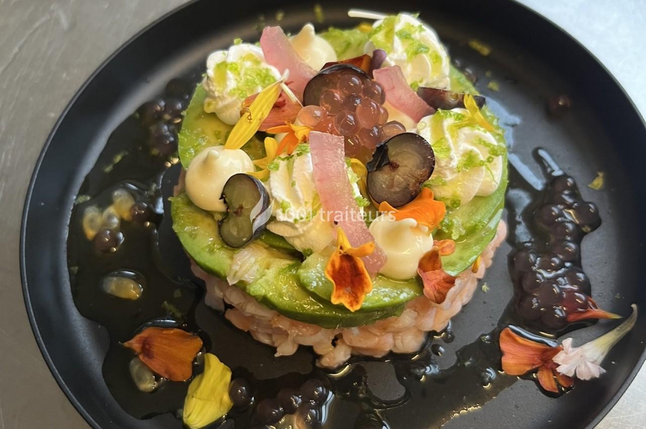Tartare de poisson surmonté d'avocat, crème, fleurs comestibles et perles de saveur, présenté dans une assiette noire.