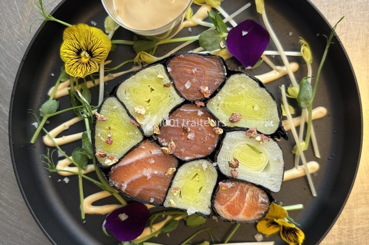Assiette de makis colorés garnis de saumon et légumes, décorée de fleurs comestibles et accompagnée d'une sauce.
