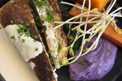 Assiette de légumes rôtis avec pommes de terre violettes, garnie de pousses fraîches et de fleurs comestibles.