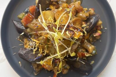 Assiette de légumes rôtis avec pommes de terre violettes, garnie de pousses fraîches et de fleurs comestibles.