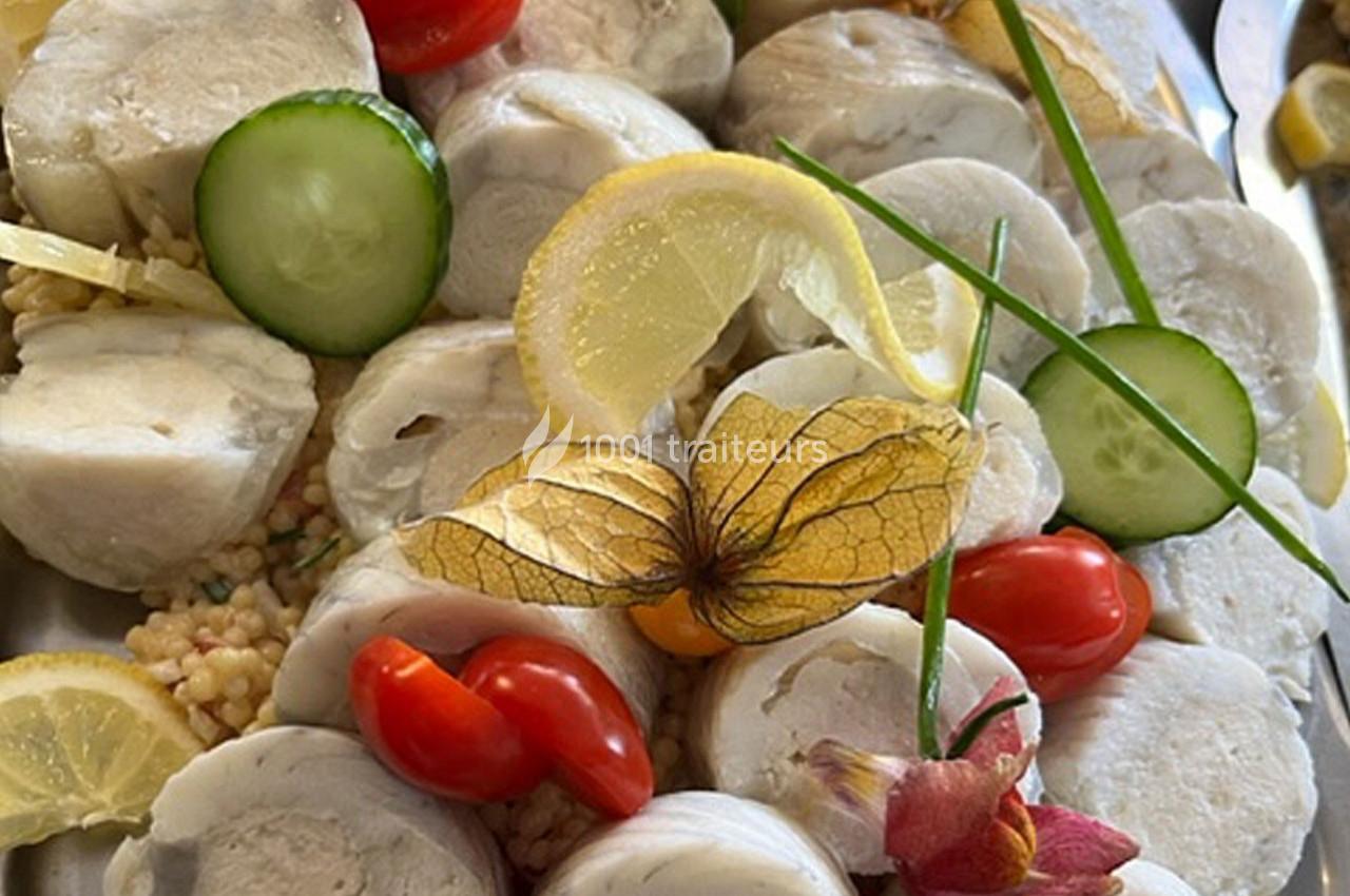 Assiette garnie de médaillons de poisson, tranches de citron, tomates cerises, rondelles de concombre et décoration florale.