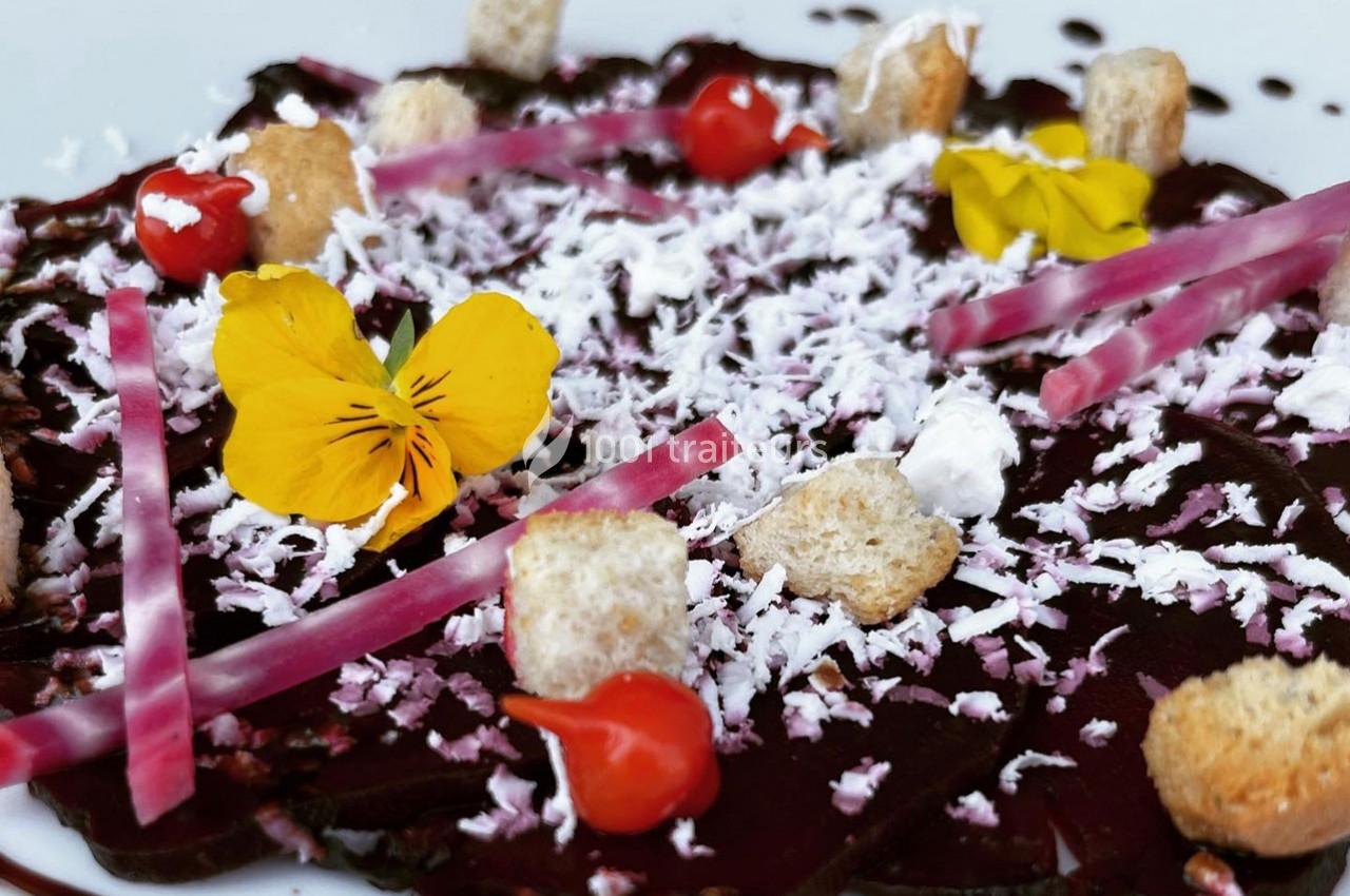 Carpaccio de betterave garni de copeaux de fromage, croûtons, fleurs comestibles et décorations colorées.