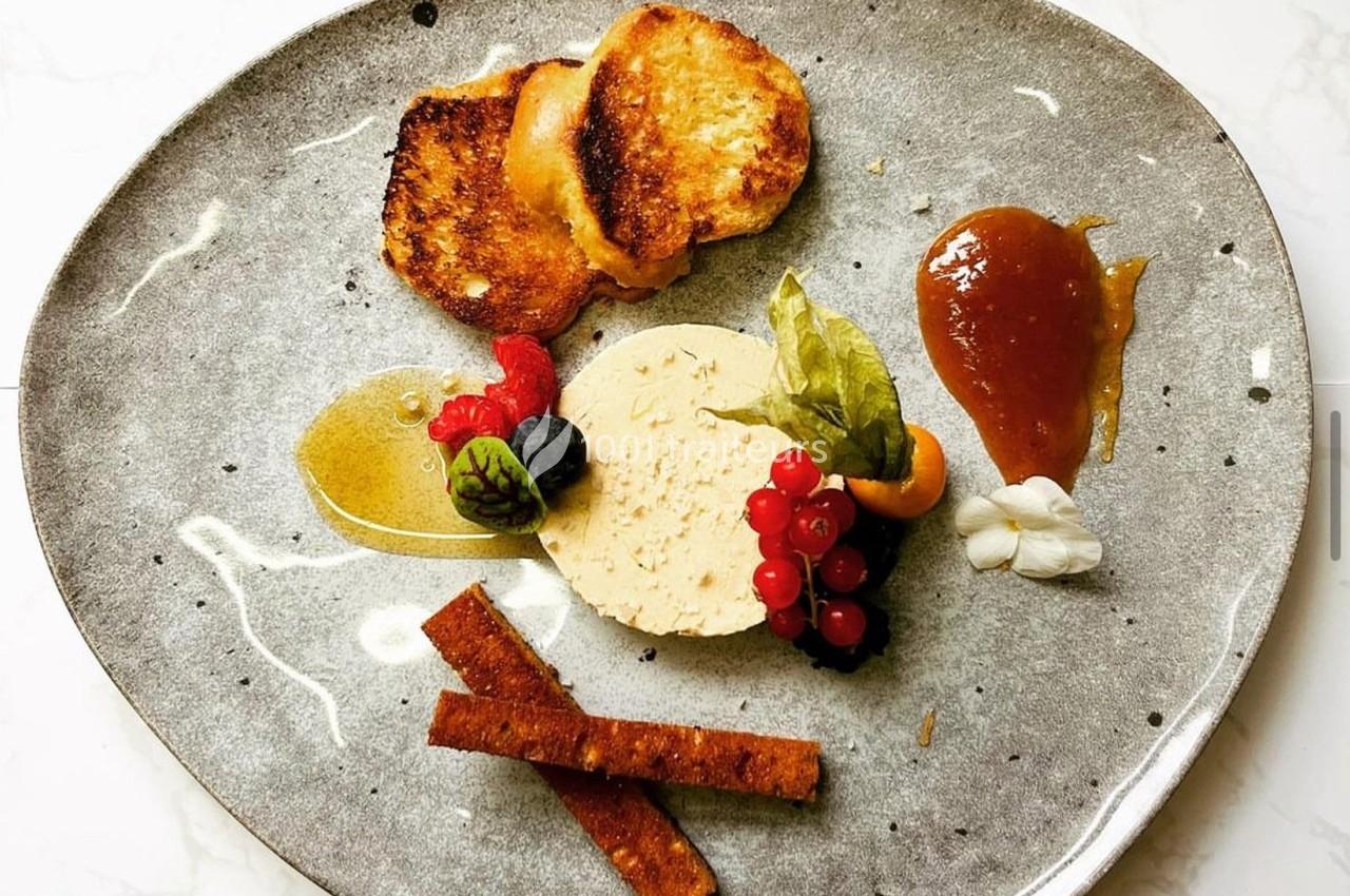 Assiette gastronomique avec foie gras, toasts, fruits rouges, chutney et garnitures sur une assiette grise.