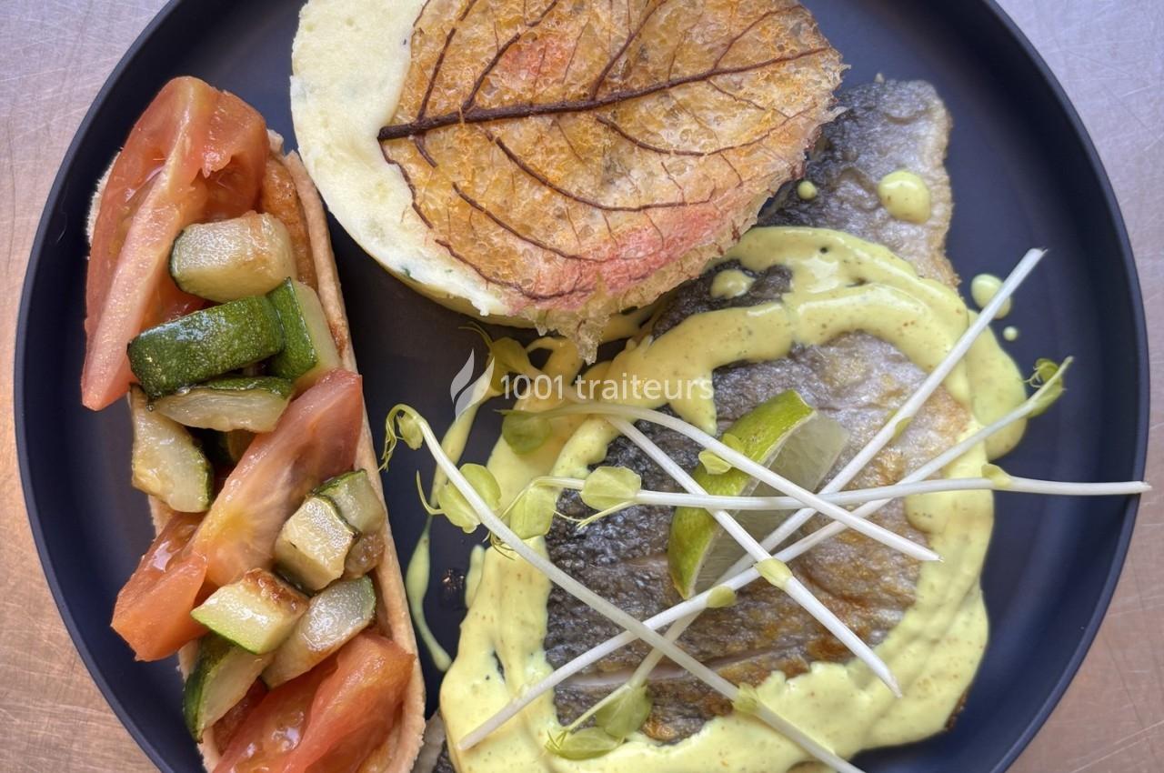 Assiette composée de poisson, purée garnie d'une feuille décorative, légumes grillés et sauce crémeuse.