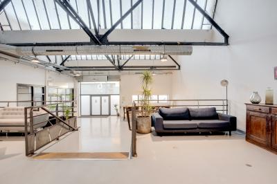 Intérieur d'un grand espace industriel lumineux avec sol clair, murs blancs, poutres métalliques et conduits apparents.