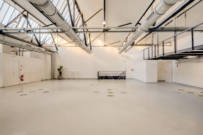 Intérieur d'un grand espace industriel lumineux avec sol clair, murs blancs, poutres métalliques et conduits apparents.