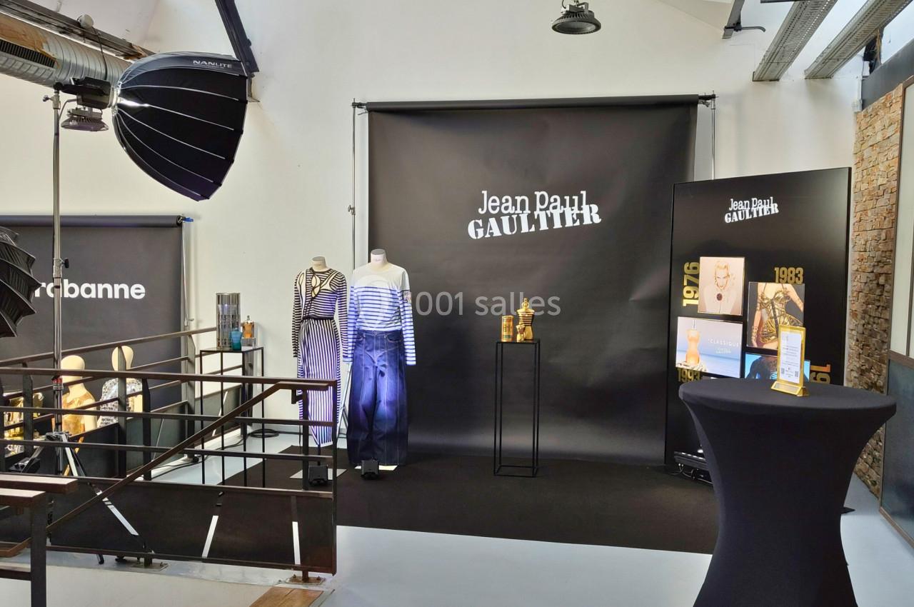 Espace d'exposition avec vêtements sur mannequins, affiches et présentoirs sous éclairage studio.