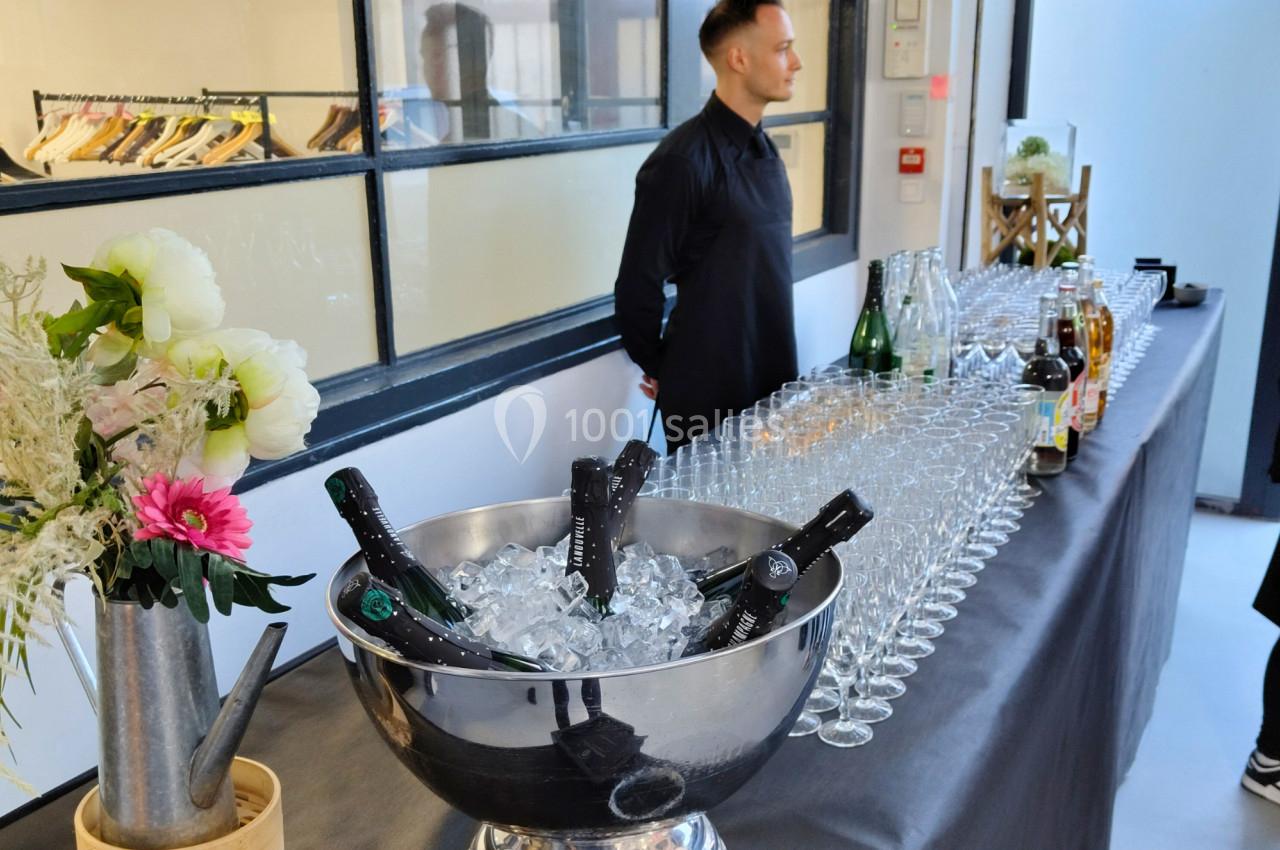 Un serveur en tenue noire près d'une table avec des bouteilles de champagne sur glace et des verres alignés.
