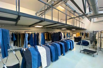 Intérieur d'un grand espace industriel lumineux avec sol clair, murs blancs, poutres métalliques et conduits apparents.