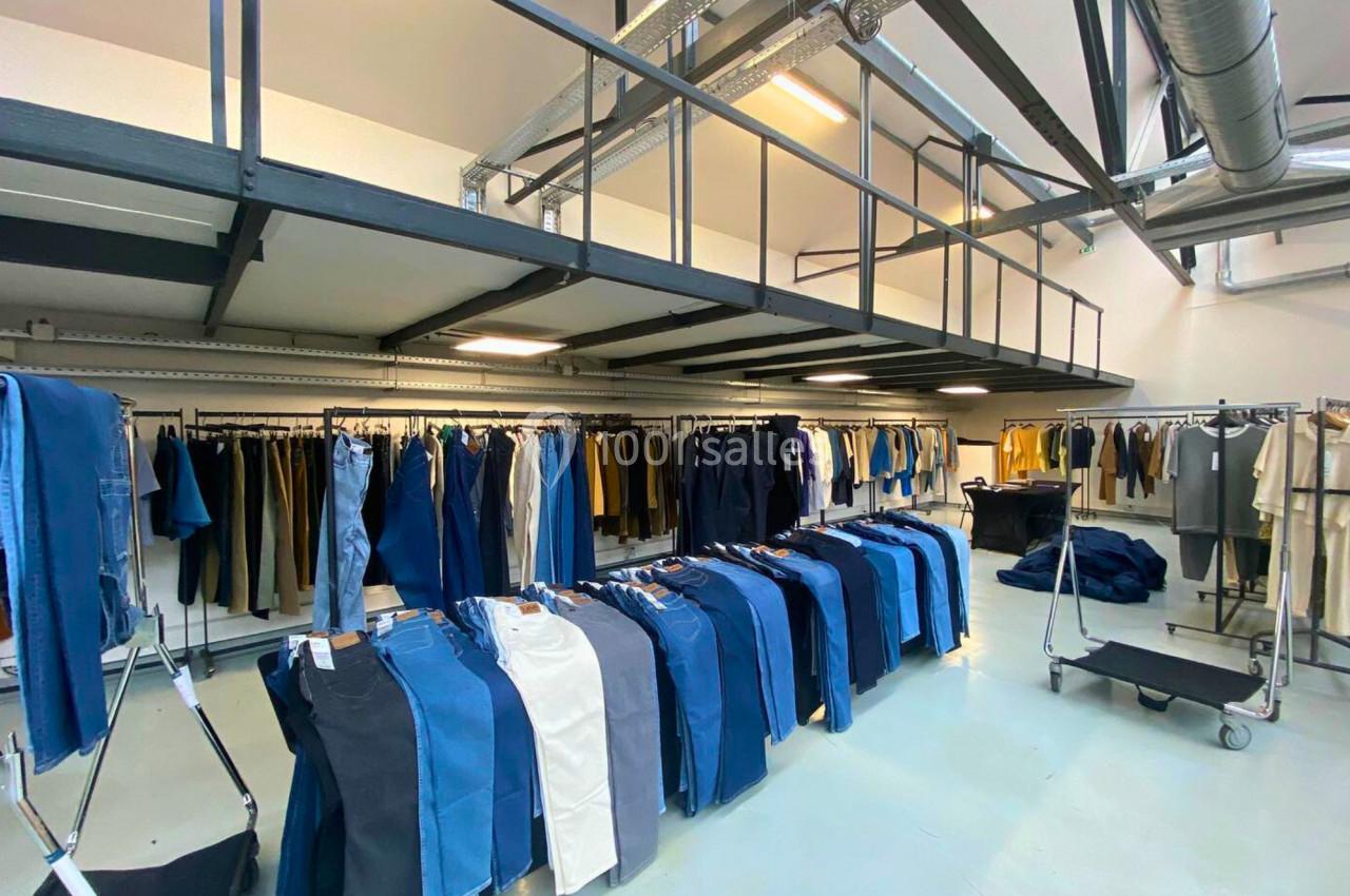 Portants de vêtements variés, principalement des jeans, exposés dans un espace lumineux et industriel.